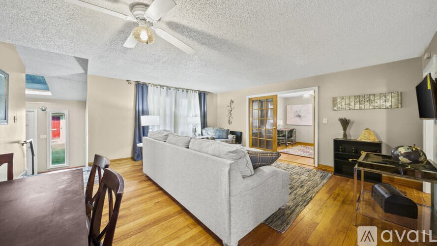 A living room with a couch, a chair, a dining table, and a ceiling fan.