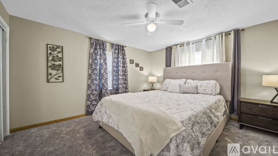 A bedroom with a large bed, a ceiling fan, and a window with curtains.