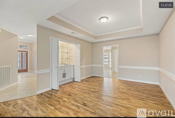 A spacious room with wooden floors and white walls, featuring a kitchenette with a sink and cabinets.
