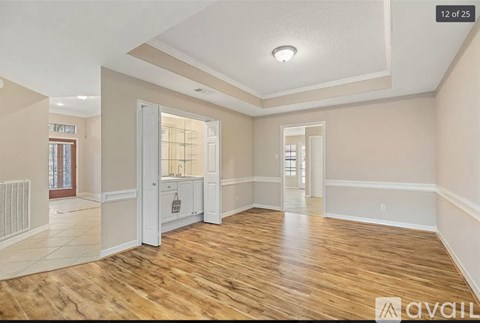 A spacious room with wooden floors and white walls, featuring a kitchenette with a sink and cabinets.