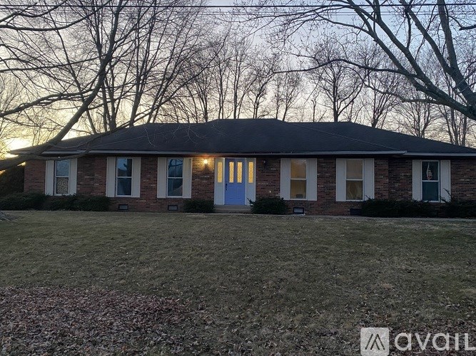 A house with a blue door is surrounded by trees and has a grassy front yard.
