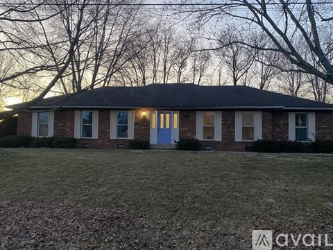 A house with a blue door is surrounded by trees and has a grassy front yard.
