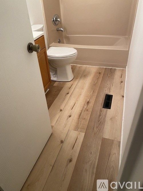 A white toilet in a small bathroom with wooden flooring.