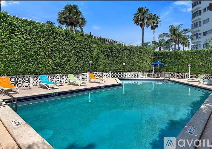 A pool surrounded by a green hedge and palm trees.