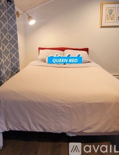 A bed with a white sheet and a red headboard with a pillow that says "QUEEN BED".