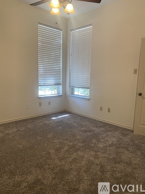 A room with a carpeted floor, two windows with blinds, and a ceiling fan with lights.