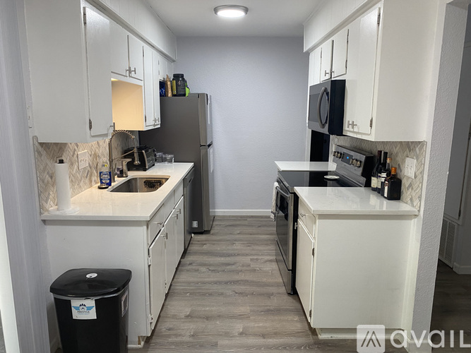 A kitchen with white cabinets and a black trash can.
