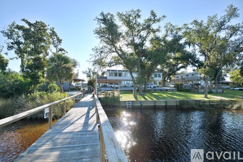 A wooden dock extends into a body of water with a house and trees in the background.