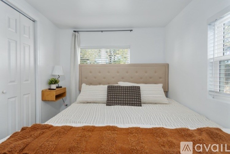 A bedroom with a bed, a nightstand with a lamp, and a window with blinds.