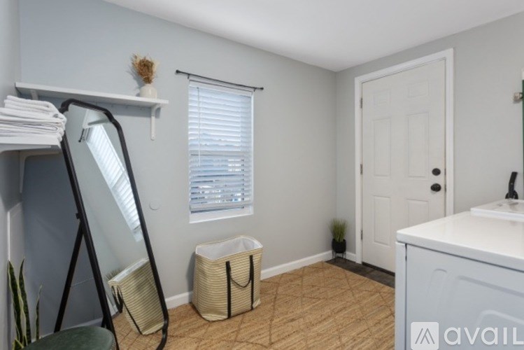 A room with a white door, a window with blinds, a mirror, and a white cabinet.