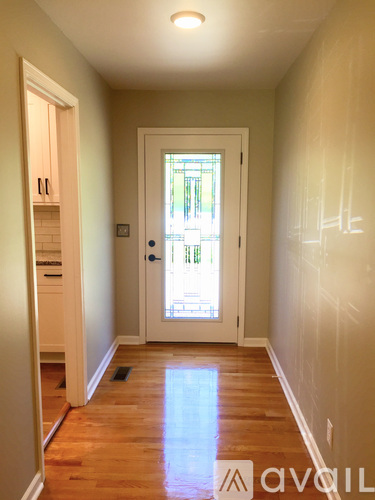 A hallway with a wooden floor and white walls leading to a door with a window.