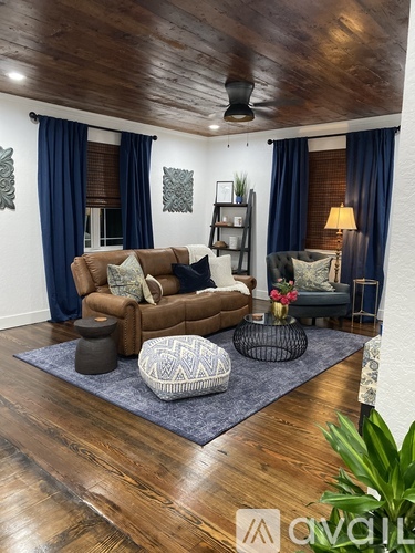 A living room with a brown couch, a grey ottoman, and a blue rug.