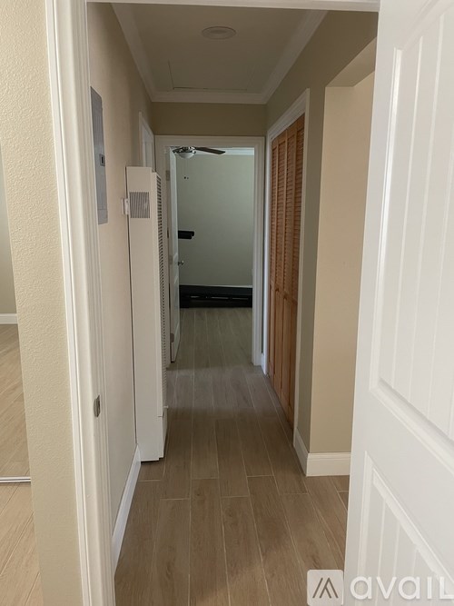 A long hallway with a door on the right and a fan on the wall.