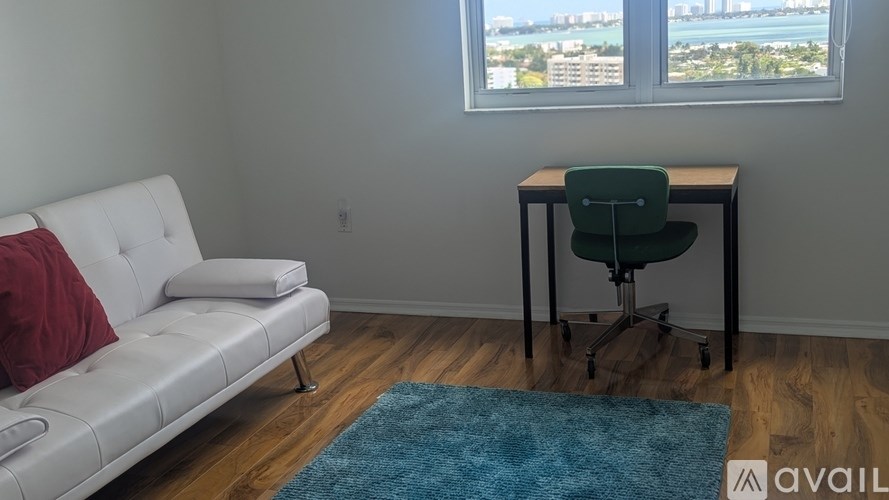A room with a white couch, a green chair, and a desk with a window overlooking a cityscape.