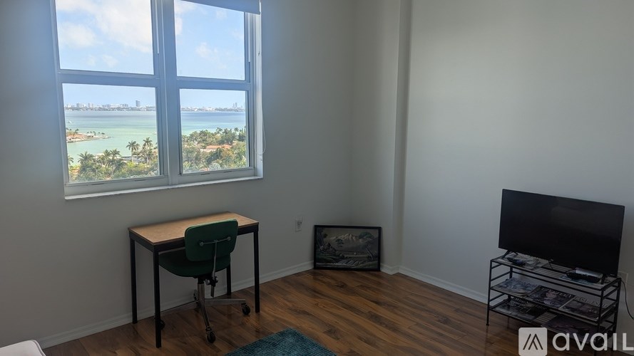 A room with a desk and a chair in front of a window overlooking a beach.