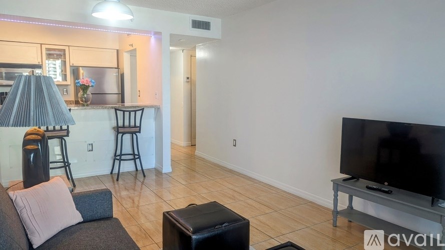 A living room with a grey couch, a black ottoman, and a flat screen TV.