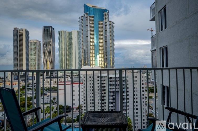 A balcony with chairs and a table overlooks a cityscape with tall buildings.