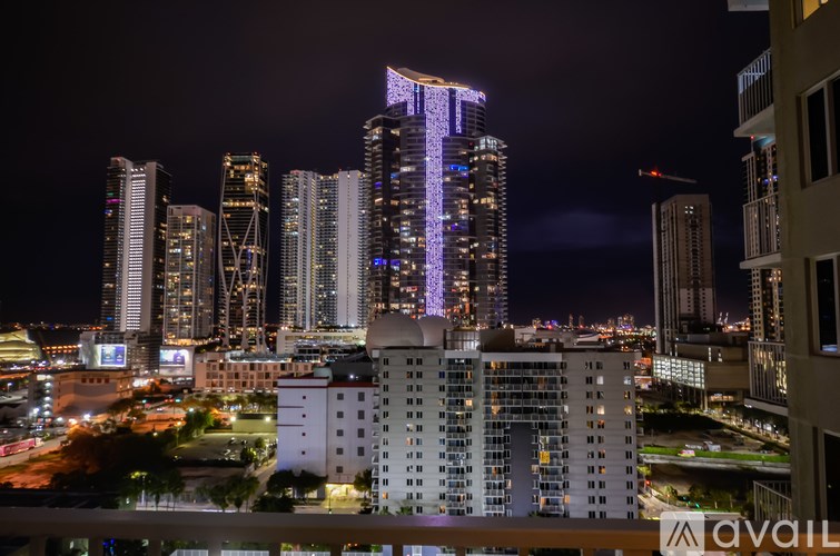 A cityscape at night with a tall building in the center illuminated with purple lights.