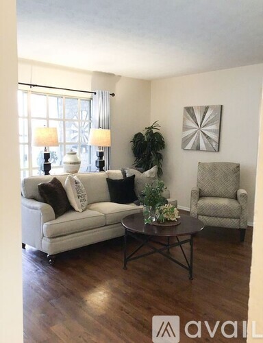 A living room with a white couch, a grey armchair, a coffee table, and a plant.