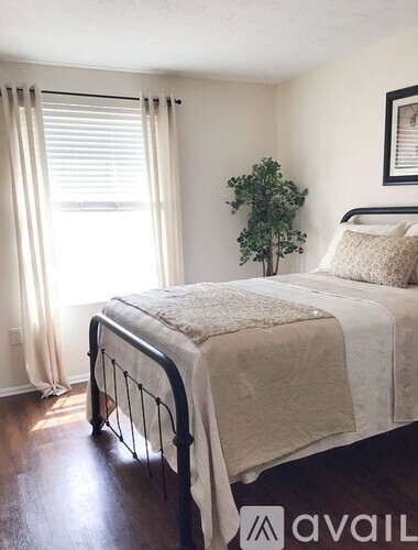 A bedroom with a bed, pillows, a plant, and a window with curtains.