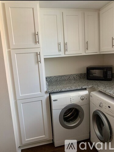 A kitchen with white cabinets and a countertop with a microwave and two washing machines.
