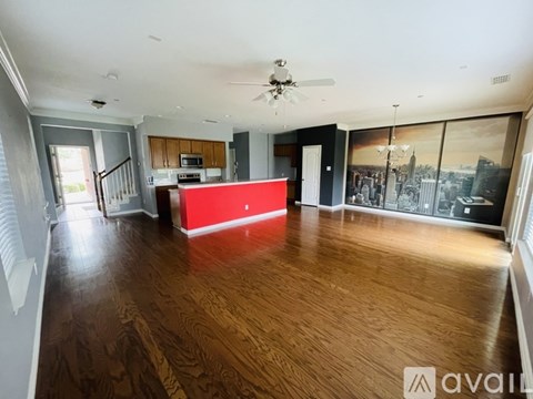 A spacious living room with a red accent wall and hardwood floors.
