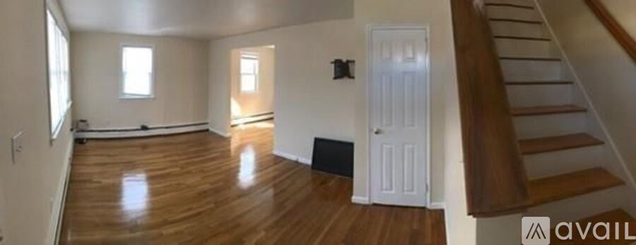 A spacious room with wooden floors and a staircase on the right side.