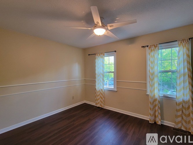 A room with a ceiling fan and two windows with curtains.