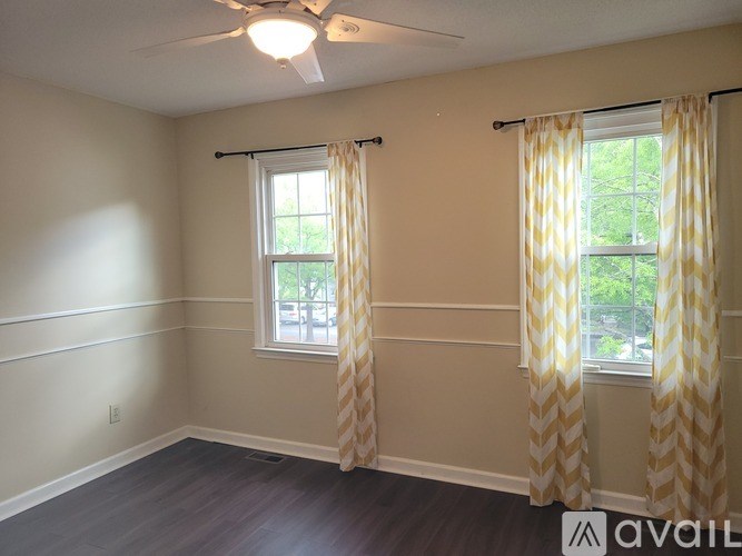 A room with a ceiling fan and two windows with curtains.