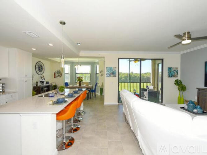 A modern kitchen with a long white table and orange chairs.