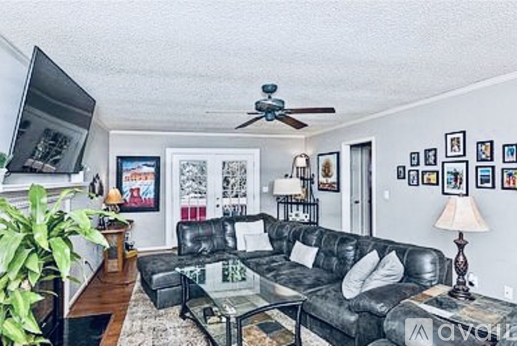 A living room with a black leather couch and a ceiling fan.