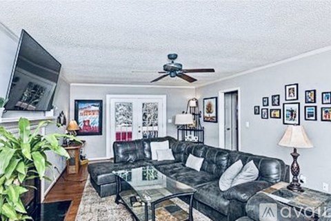 A living room with a black leather couch and a ceiling fan.