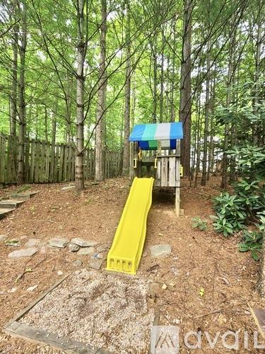 A playground with a yellow slide in the middle of a wooded area.