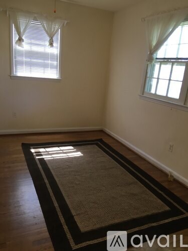 A room with a rug on the floor and two windows with curtains.