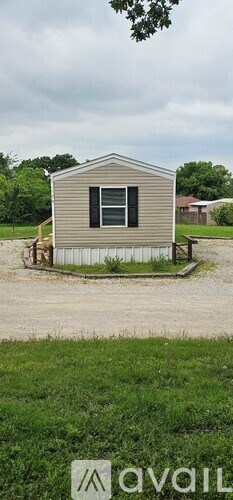 A small house with a brown roof and a grey wall is situated in a grassy area.