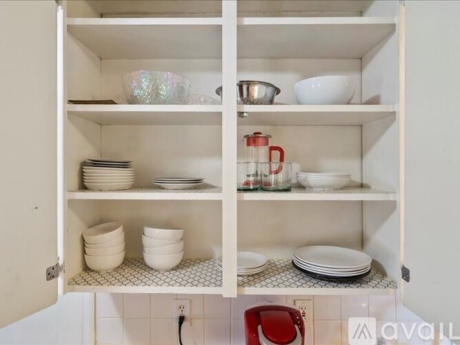 A kitchen cabinet with white shelves holding various dishes and bowls.