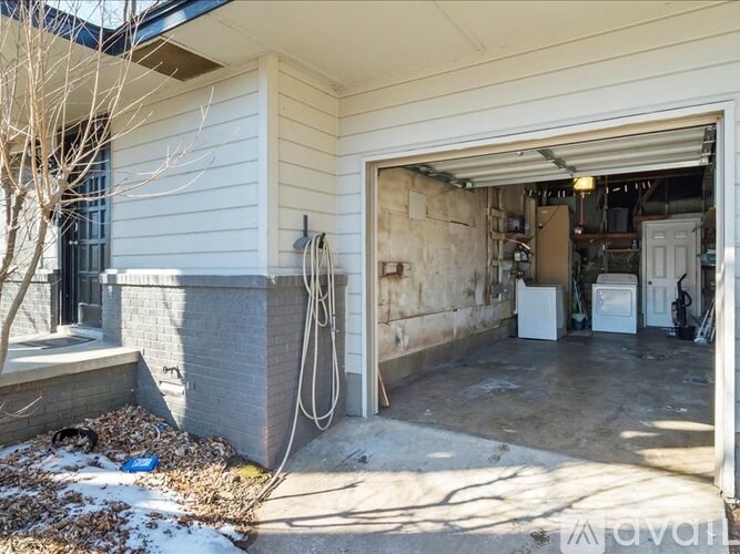 A garage with a white door is open, revealing a cluttered interior.