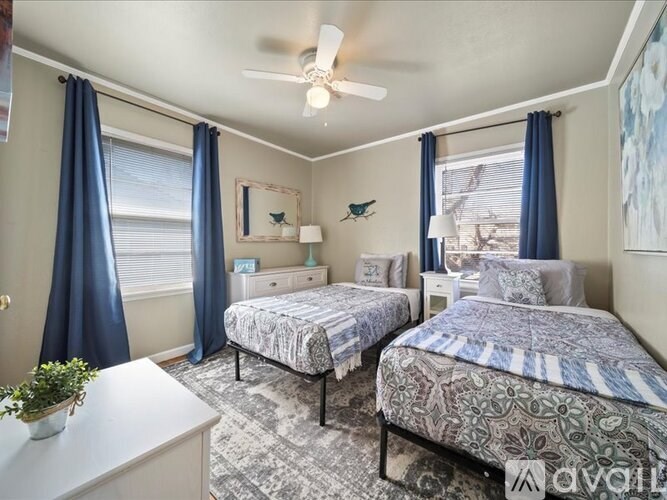 A bedroom with two beds, a ceiling fan, and a window with blue curtains.