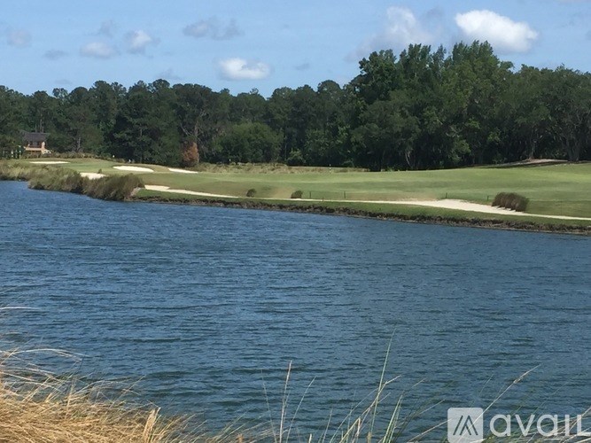 A golf course with a body of water in the foreground and trees in the background.