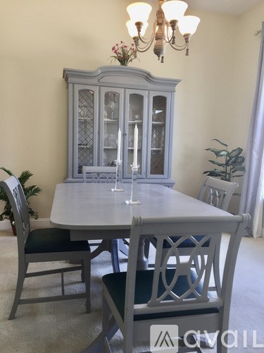 A grey dining table with chairs and a cabinet with glass doors.