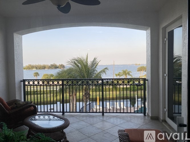 A balcony with a table and chairs overlooking a pool and palm trees.
