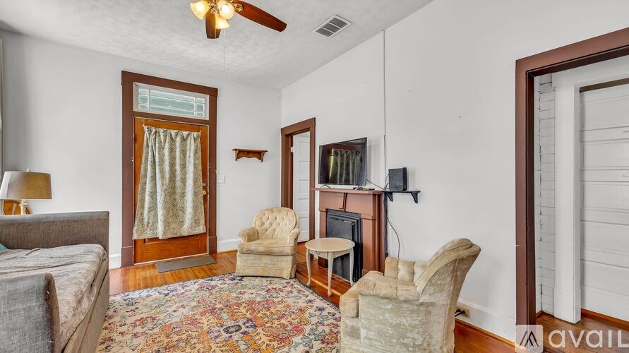 A living room with a grey couch, a rug, a chair, a television and a fan.