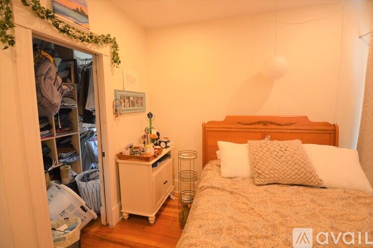 A bedroom with a bed, nightstand, and a closet with clothes.