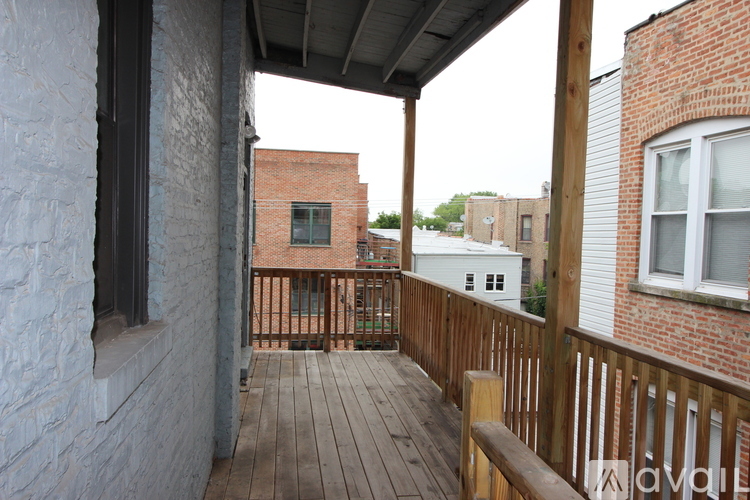 A wooden deck with a bench and a brick building in the background.