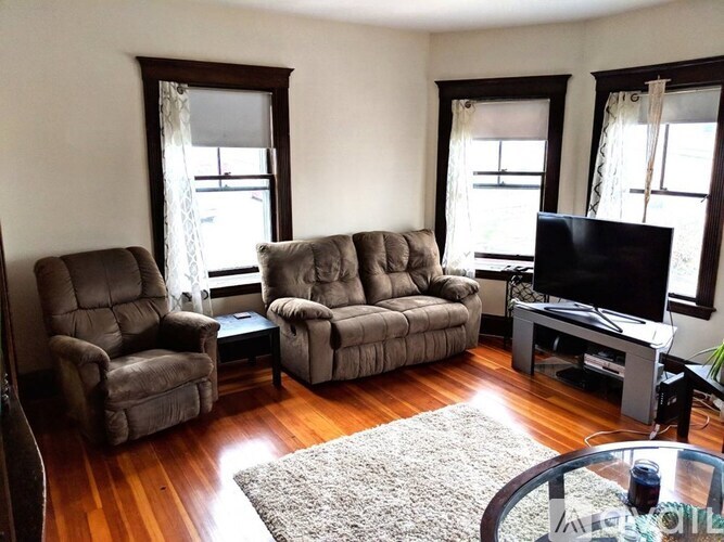 A living room with a grey couch, a brown chair, a television, and a glass table.