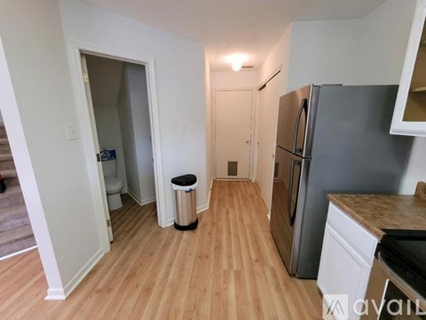 A kitchen with a refrigerator, wooden floors, and a trash can.
