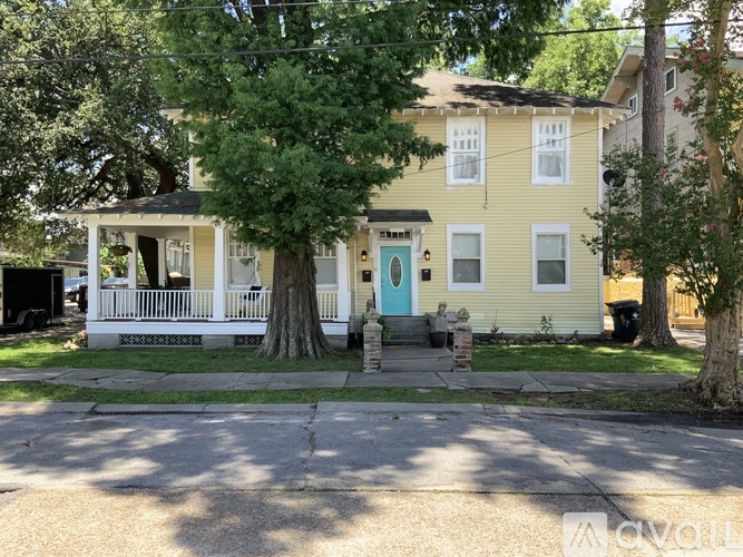 A yellow house with a blue door and a tree in front.