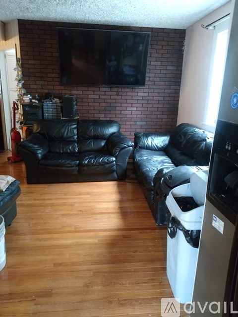 A living room with black leather furniture and a flat screen TV mounted on a brick wall.