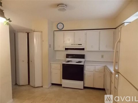 A kitchen with white cabinets and appliances, a clock on the wall, and a tiled floor.