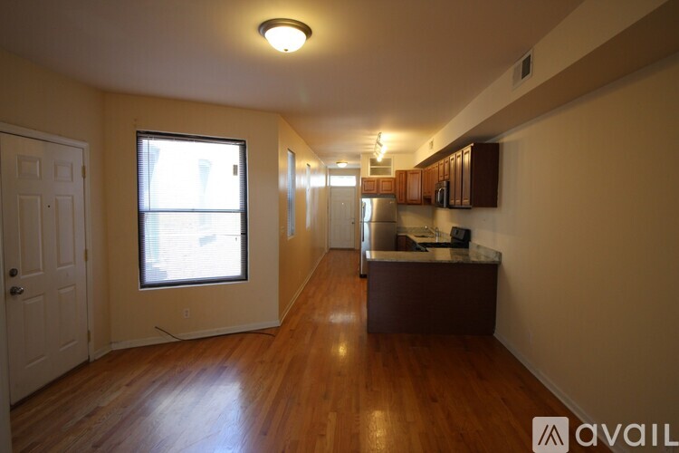A spacious room with wooden floors and a kitchen area in the background.